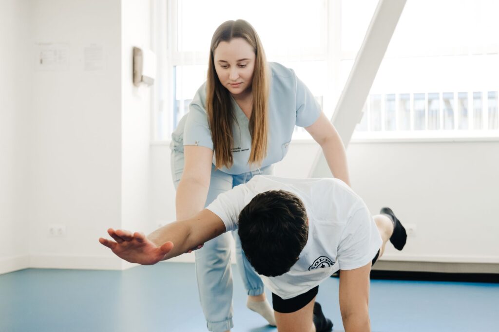 Une kinésithérapeute accompagne un patient lors d’un exercice d’équilibre à quatre pattes en rééducation.