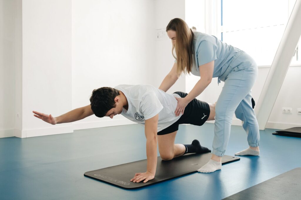Une physiothérapeute accompagne un homme dans un exercice de stabilisation du dos sur un tapis.