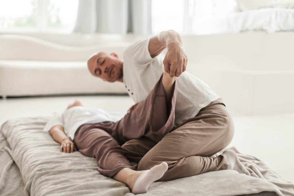 Un praticien accompagne l’étirement de la jambe d’une personne allongée sur un matelas pour travailler sa mobilité.