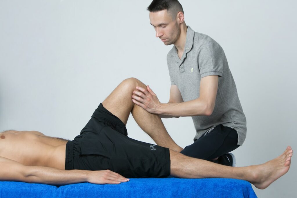 Un physiothérapeute mobilise le genou fléchi d’un homme allongé sur une table de soin.
