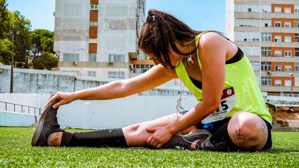 Coureuse assise sur une pelouse, étirant sa jambe dans le cadre d’un retour à la course après une blessure
