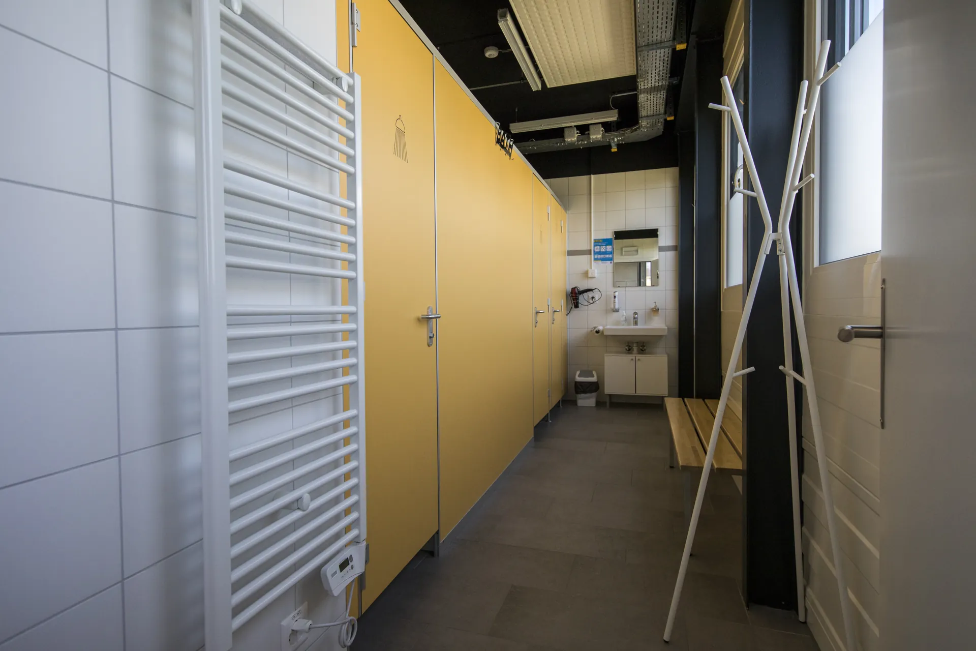 Vestiaire du centre VO2Sport avec cabines de douche jaunes, banc en bois et lavabo