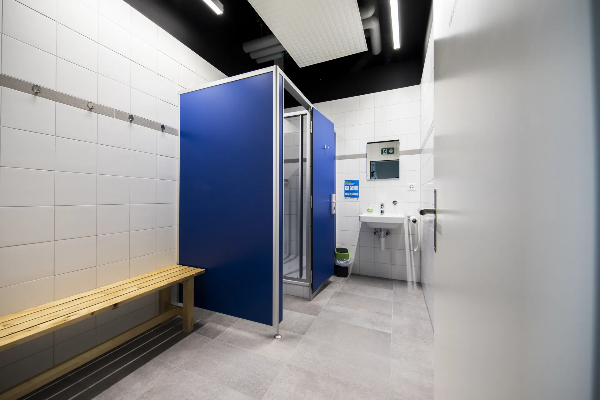 Vestiaire du centre VO2Sport avec banc en bois, cabine de douche bleue et lavabo.